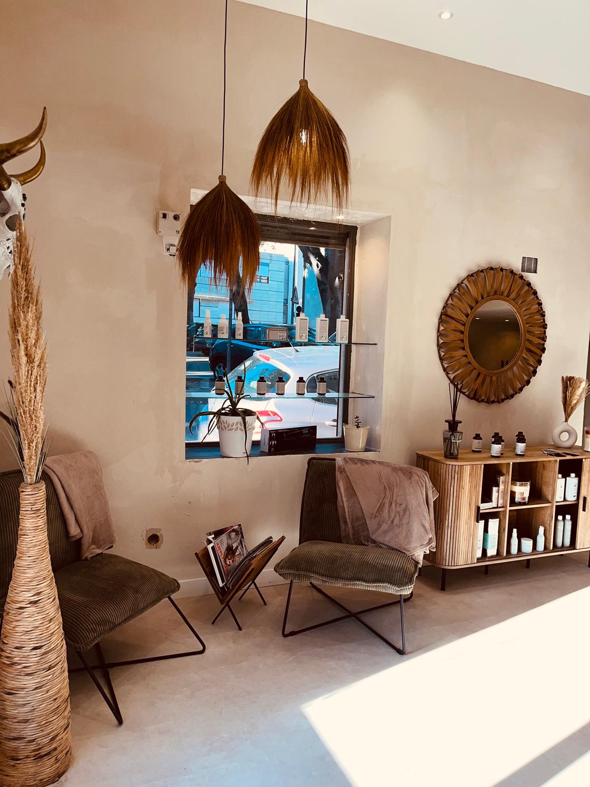 Espace d’attente de Maison Mégane, avec deux fauteuils, un meuble en bois et des suspensions en fibres naturelles.