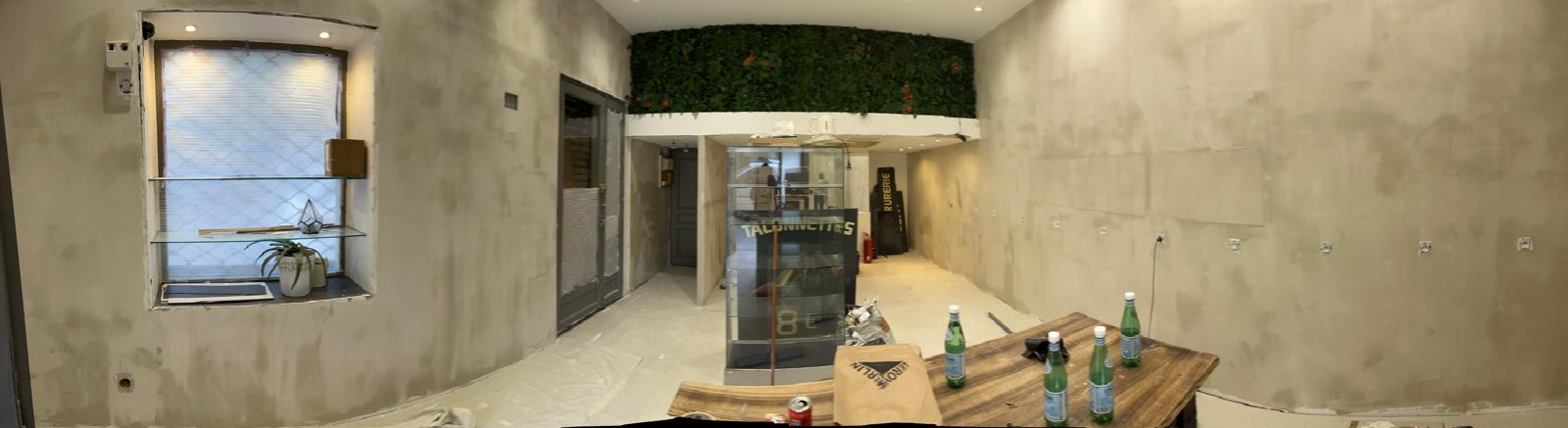 Vue panoramique du local Maison Mégane pendant les travaux, montrant les murs en préparation et le décor végétal.