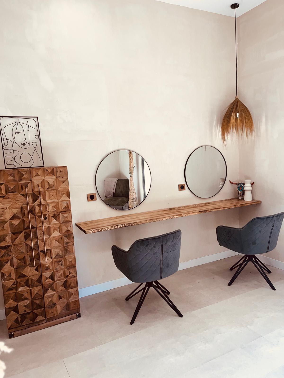 Deux postes de coiffure du salon Maison Mégane, avec des miroirs ronds, une tablette en bois et des murs aux teintes douces.